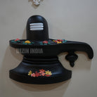 Black Shiva Lingam with colorful flowers on a white wall, branded 'Dezin India'.
