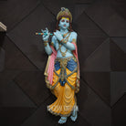 Colorful statue of a deity holding a flute against a dark geometric-patterned background